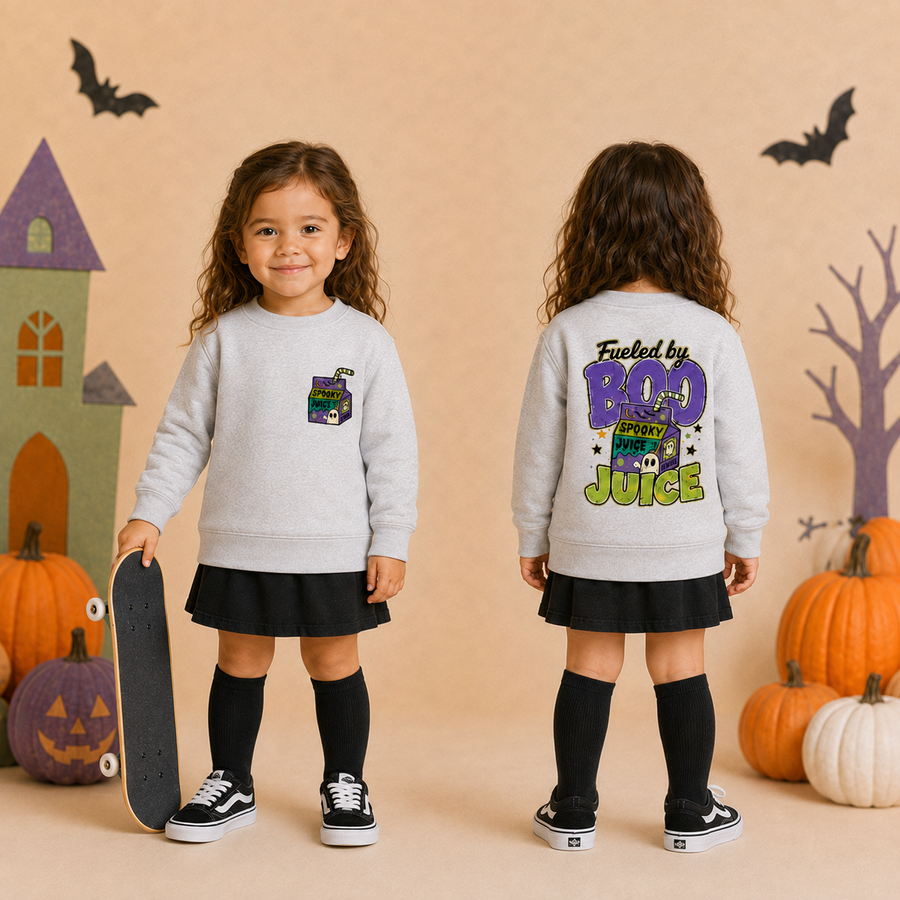 A toddler girl is shown from the front and back wearing a light gray sweatshirt with a Halloween-themed graphic. The front has a small purple juice box graphic on the left chest, and the back features a large graphic reading 'Fueled by BOO Juice' in purple, green, and yellow.