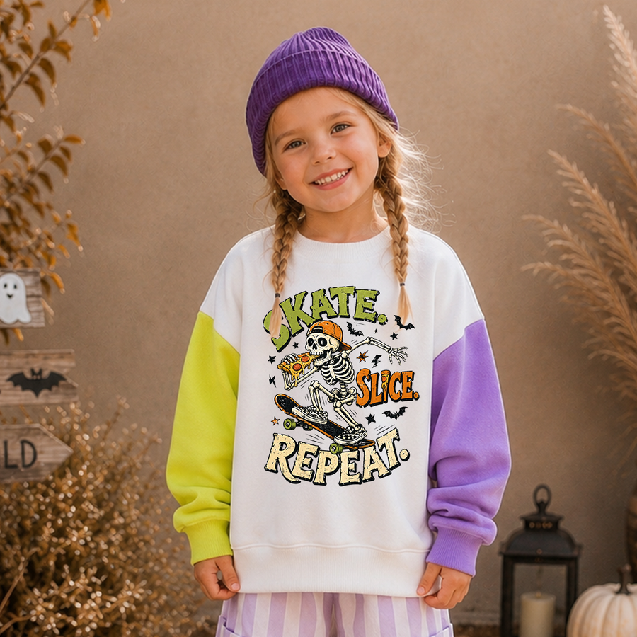 A young girl with braided hair wears a white sweatshirt with purple and neon yellow color-block sleeves and a Halloween graphic that reads 'Skate, Slice, Repeat.' She is also wearing a purple beanie and striped pants, standing in a styled outdoor setting with warm neutral background elements.